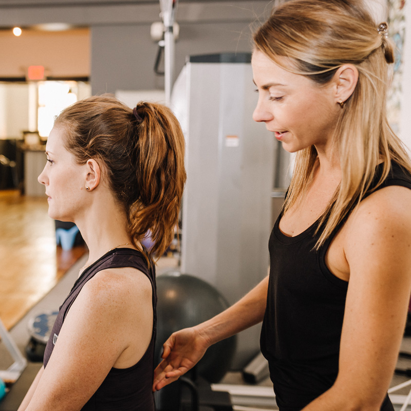 A Sanctuary Body pilates instructor adjusts her client's posture