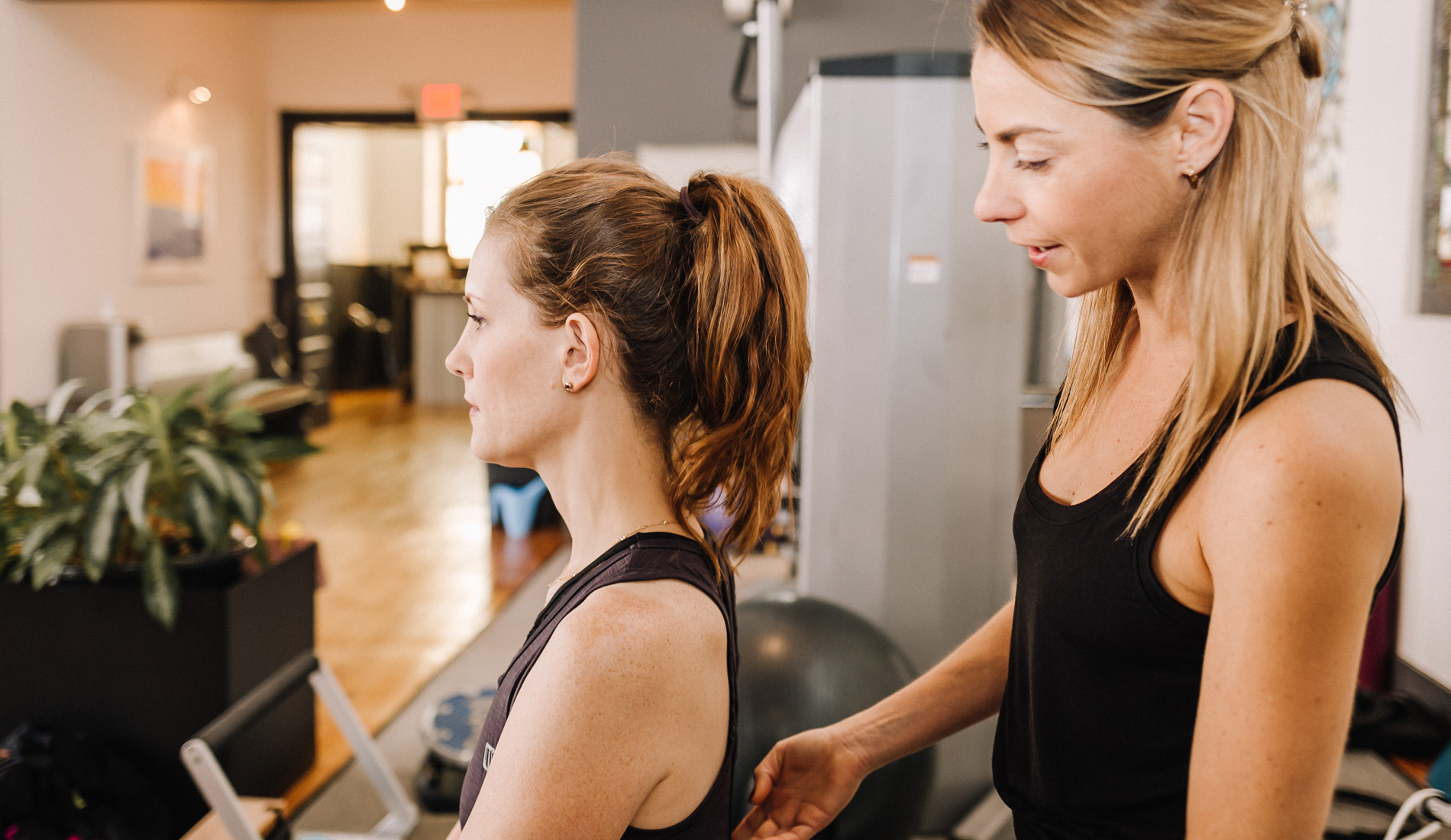 A Sanctuary Body Pilates instructor adjusts her client's posture